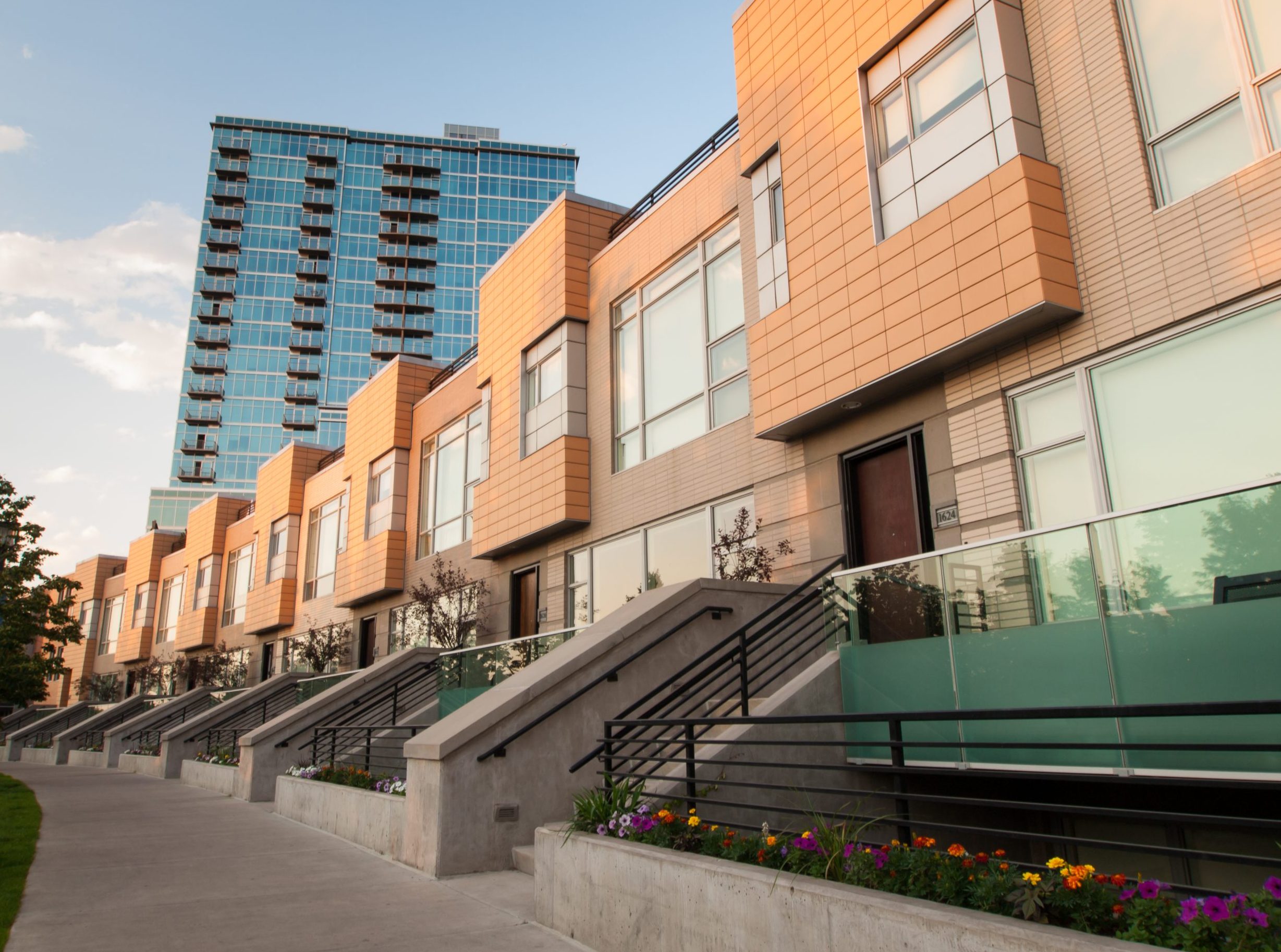 Modern townhomes with glass railings and a high-rise building in the background, located in Denver, Colorado.