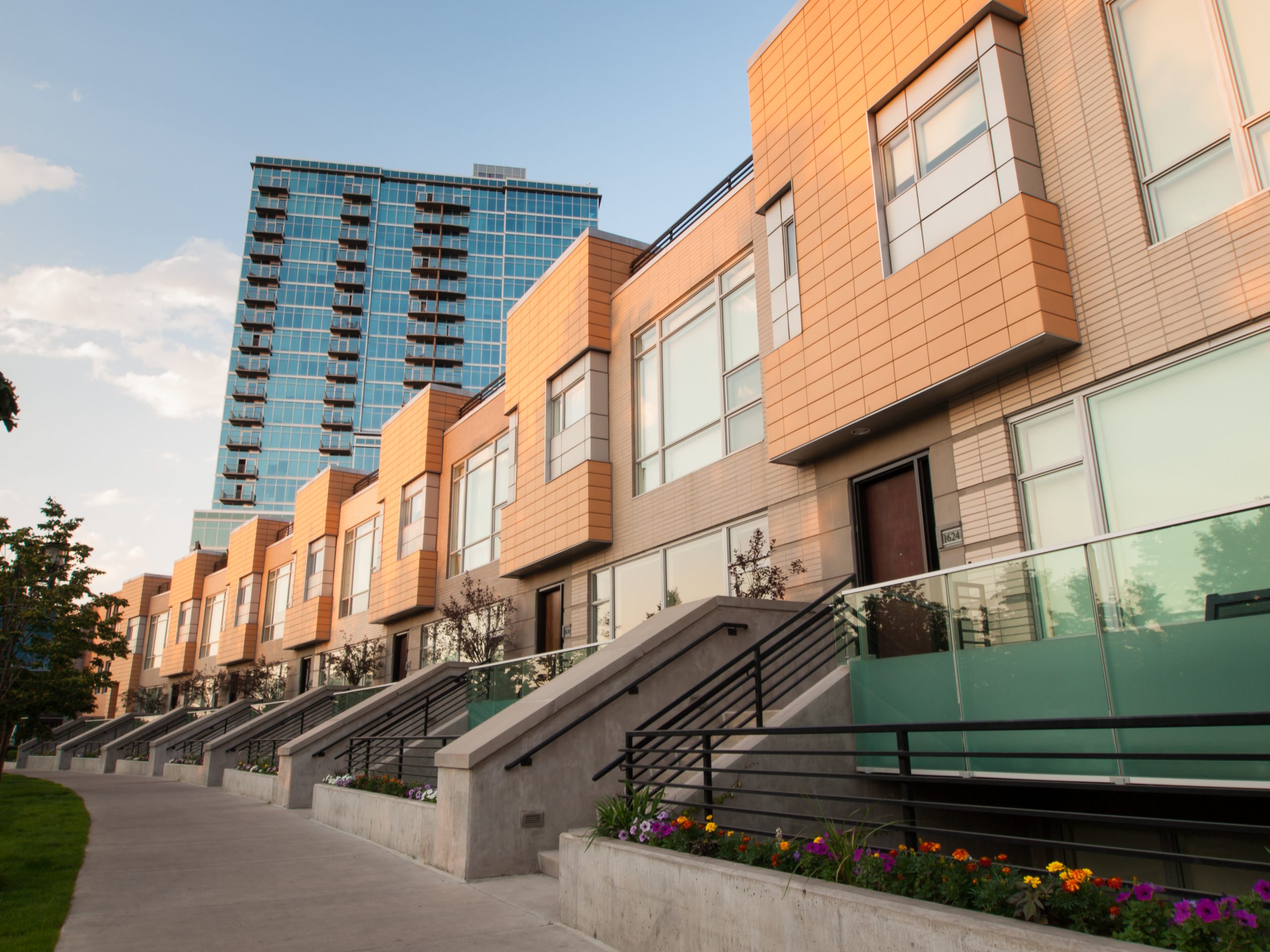 Modern townhomes with glass railings and a high-rise building in the background, located in Denver, Colorado.