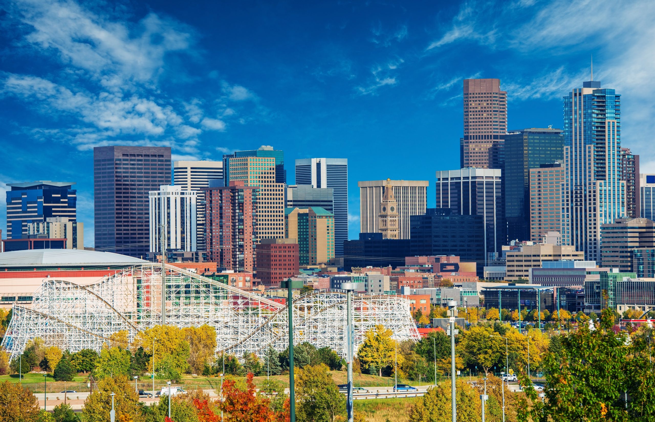 Downtown Denver skyline with Elitch Gardens amusement park and modern skyscrapers under a vibrant blue sky.