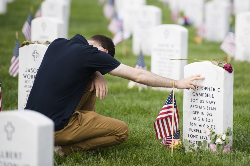 Man kneeling at the grave of a fallen U.S. Navy service member during Memorial Day at Arlington National Cemetery, honoring their sacrifice.
